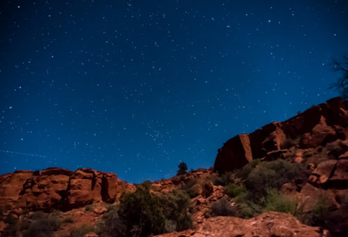 A starry night sky over rugged red rock formations, illuminated by a soft blue glow.