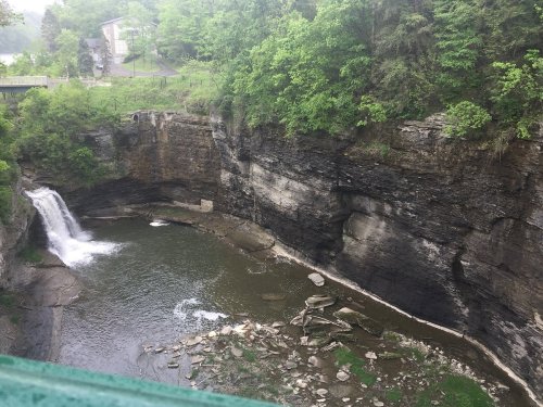 A serene waterfall cascades into a rocky pool, surrounded by lush greenery and steep cliffs.