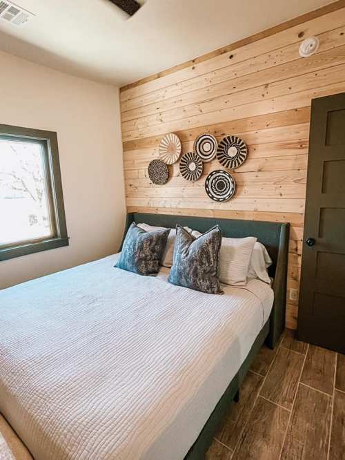 Cozy bedroom featuring a bed with decorative pillows, wooden accent wall, and circular wall art.