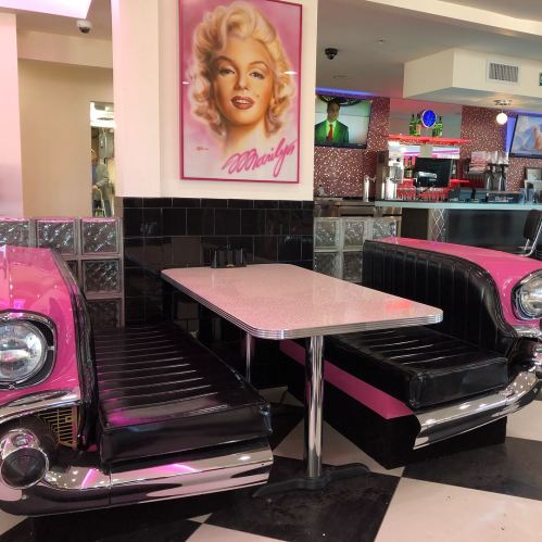 A retro diner booth with pink and black seating, featuring a table and a Marilyn Monroe portrait on the wall.