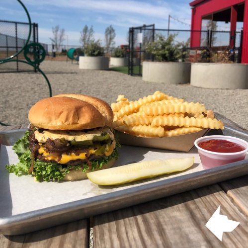 A juicy burger with lettuce, cheese, and pickles, served with crinkle-cut fries and a side of ketchup on a tray.