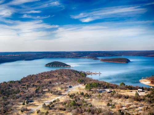 A scenic view of a lake surrounded by islands and trees under a blue sky with wispy clouds.