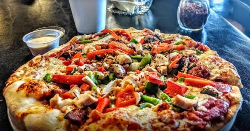 A close-up of a colorful pizza topped with vegetables and chicken, served with a side of dipping sauce.