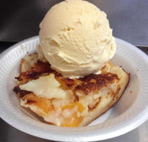 A slice of peach cobbler topped with a scoop of vanilla ice cream in a white bowl.