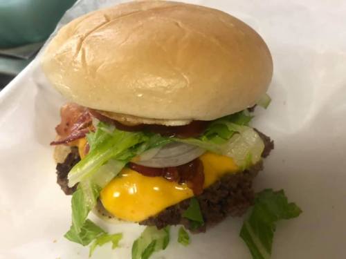 A close-up of a cheeseburger with lettuce, bacon, onions, and a soft bun on a white background.