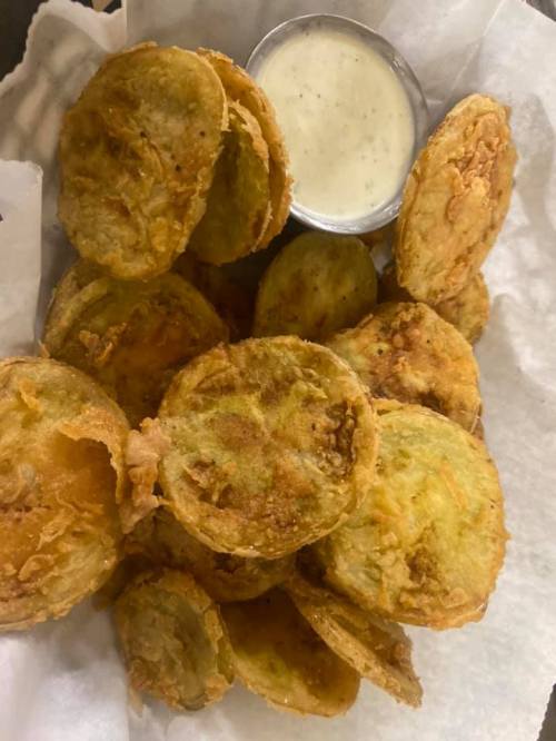 A basket of crispy fried green tomatoes served with a small cup of dipping sauce.