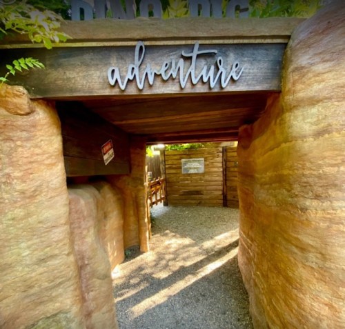 A rustic entrance with the word "adventure" above, leading into a gravel path surrounded by stone walls.