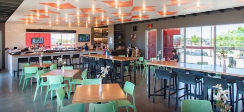 Bright, modern restaurant interior with colorful decor, tables, and a bar area. Patrons are seated and enjoying their meals.