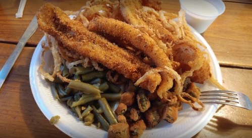 A plate of fried fish fillets, crispy onion rings, and green beans served with a small cup of dipping sauce.