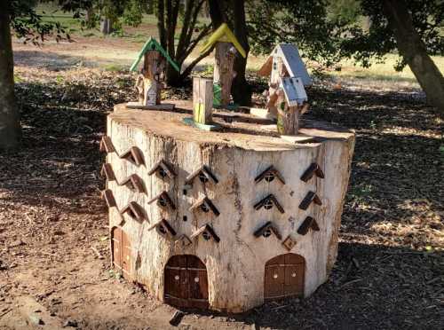 A whimsical tree stump with miniature houses and birdhouses, set in a natural outdoor environment.