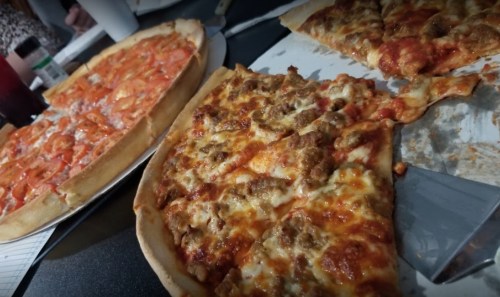 Two pizzas on a table, one with pepperoni and the other with sausage, with a slice removed from the sausage pizza.
