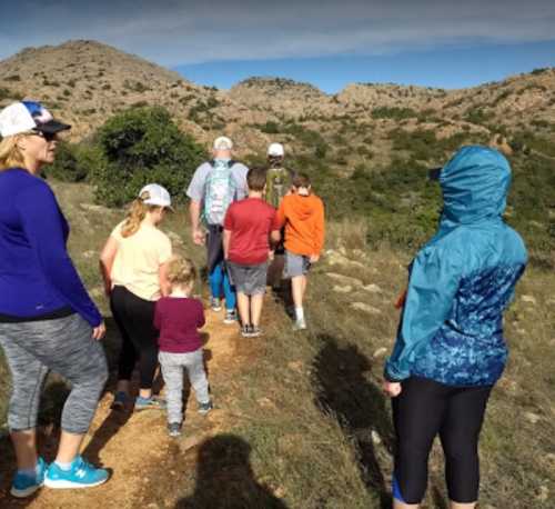 A group of people hiking on a trail in a mountainous area, wearing casual outdoor clothing and hats.