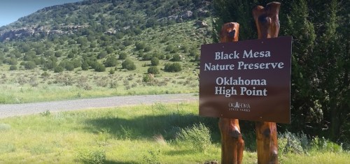 Sign for Black Mesa Nature Preserve in Oklahoma, surrounded by greenery and mountains in the background.