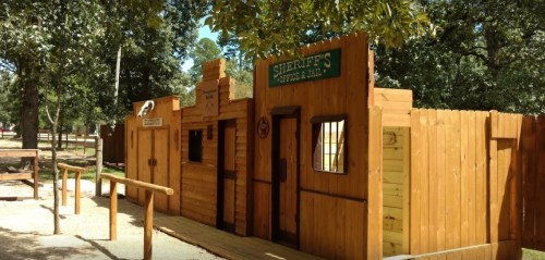 A wooden western-style building with signs for a sheriff's office and a general store, surrounded by trees.