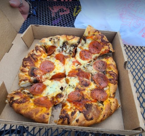 A partially eaten pizza with pepperoni and mushrooms in a cardboard box on a table.