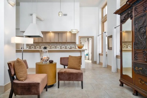 Modern living space featuring two brown chairs, a round table, and an ornate cabinet against a bright, airy backdrop.