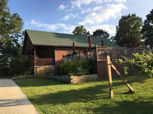 A wooden building with a green roof, featuring a deck and outdoor seating, surrounded by trees and grass.