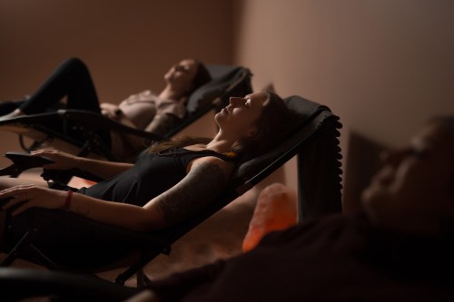 Three people relax in reclining chairs, eyes closed, in a softly lit room.