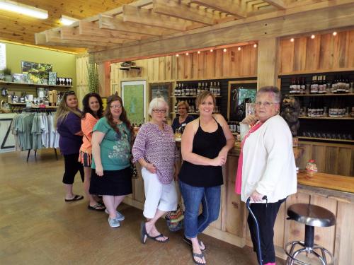 A group of seven women stands together in a rustic shop, smiling and posing for the camera.