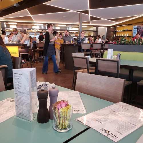 A busy restaurant interior with tables set for dining, patrons walking, and a vibrant atmosphere.