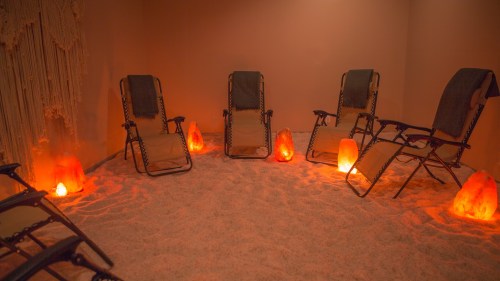 A serene room with five reclining chairs, surrounded by glowing salt lamps and a sandy floor, creating a calming atmosphere.