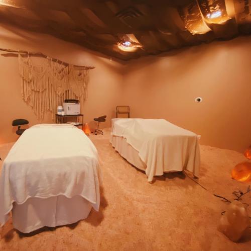 A serene spa room with two massage tables, soft lighting, and earthy decor, creating a calming atmosphere.