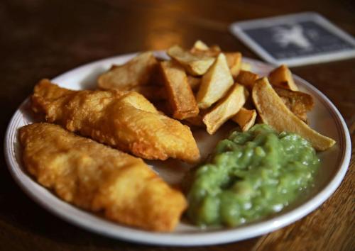 A plate of golden-brown fish fillets, crispy chips, and a serving of green mushy peas.