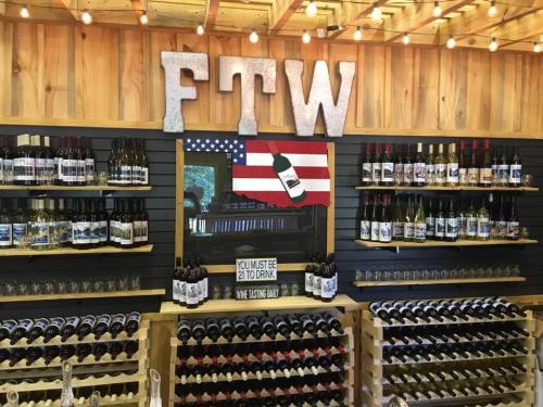A wooden wine display featuring various bottles, with a sign reading "FTW" and an American flag backdrop.