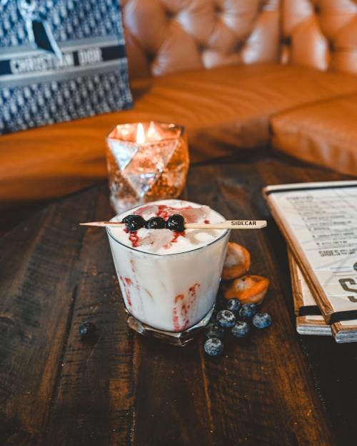 A dessert in a glass topped with berries, served on a wooden table with a candle and menu in the background.