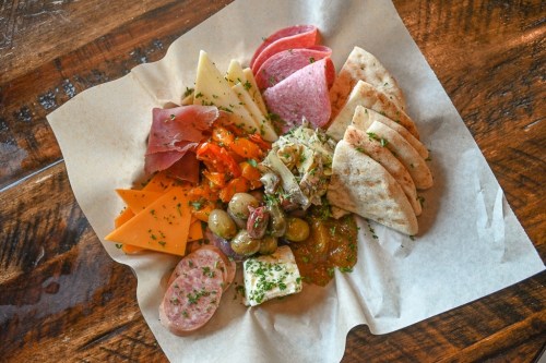 A platter of assorted meats, cheeses, olives, and pita bread, garnished with herbs on a wooden table.