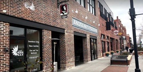 Exterior view of a brick building featuring Andolini's Pizzeria and nearby storefronts, with benches and planters.