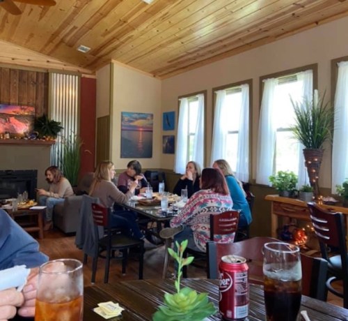 A cozy café interior with patrons chatting, enjoying drinks, and surrounded by plants and natural light.