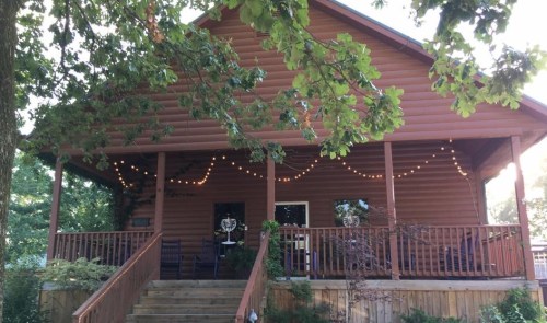 A cozy wooden cabin with a porch, surrounded by trees and string lights, creating a warm, inviting atmosphere.