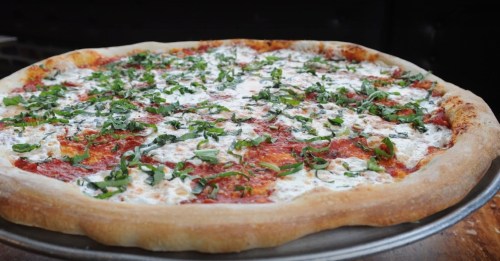 A freshly baked pizza topped with cheese and sprinkled with green herbs on a metal tray.
