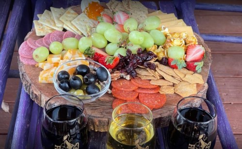 A wooden platter filled with assorted cheeses, meats, fruits, nuts, and crackers, accompanied by two glasses of wine.