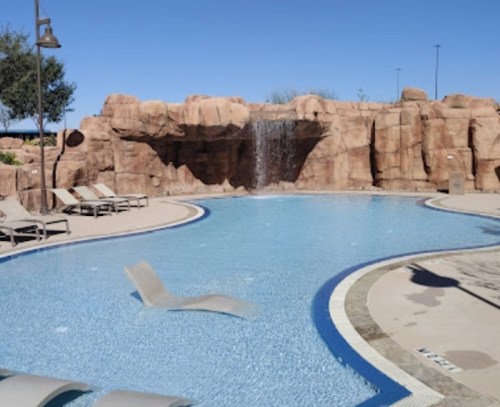 A serene pool area with a rock waterfall, lounge chairs, and a clear blue sky in the background.