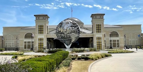 Exterior view of a large building with a globe sculpture, labeled "Mystic World Casino," surrounded by greenery.
