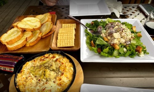 A table setting with a baked dish, a fresh salad, crackers, and toasted bread.