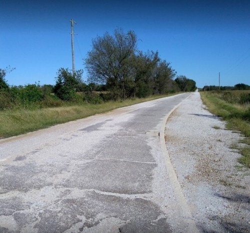 A quiet, empty road lined with greenery under a clear blue sky.