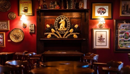 Cozy pub interior with wooden tables, a decorative fireplace, and vintage wall art in warm lighting.