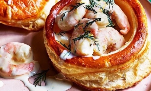 A flaky pastry shell filled with shrimp and topped with dill, served with a creamy sauce on the side.