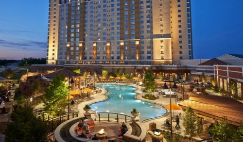 A luxurious hotel with a large pool area, surrounded by trees and lounge chairs, illuminated at dusk.