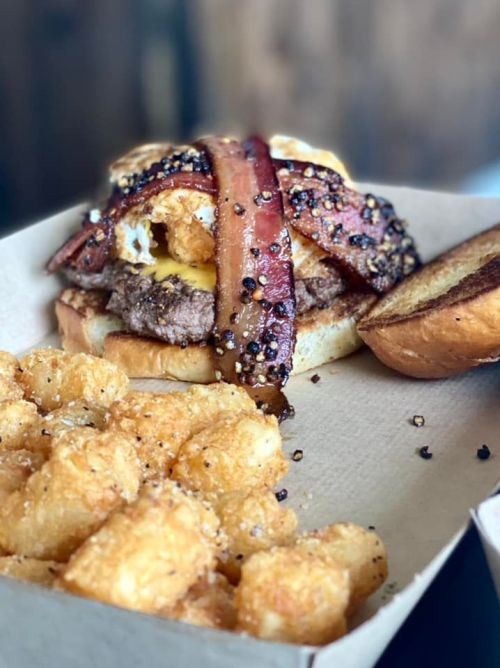 A hearty burger topped with bacon, cheese, and an egg, served with crispy tater tots on the side.