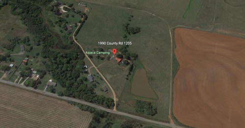 Aerial view of a rural area featuring a camping site labeled "Alpaca Camping" near fields and homes.