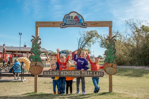 A group of five children smiles and poses with their arms raised at a sign that reads "Making Memories That Last."