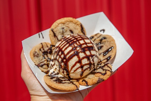 A hand holding a bowl of cookie cups filled with ice cream, drizzled with chocolate sauce, against a red background.