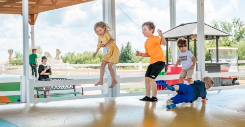 Children playing and jumping on a bouncy surface at an outdoor facility, with adults observing in the background.