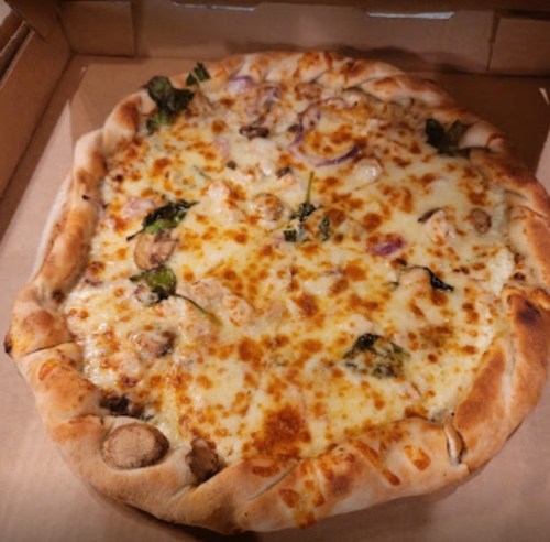 A freshly baked pizza with melted cheese, mushrooms, and green toppings in a pizza box.
