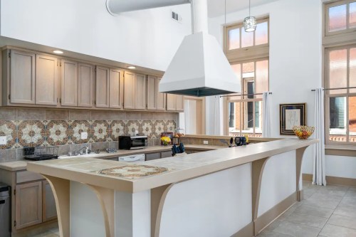 Bright kitchen with light wood cabinets, decorative tile backsplash, and a central island with a modern range hood.