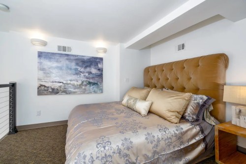 Cozy bedroom featuring a tufted headboard, decorative pillows, and abstract wall art. Soft lighting enhances the ambiance.